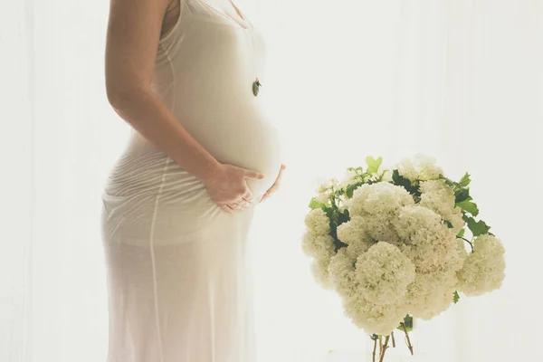 Jonge mooie zwangere vrouw staat in de buurt van raam thuis — Stockfoto