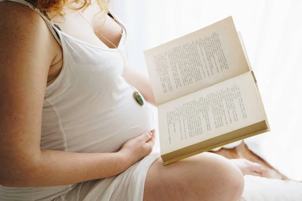 Schwangere berührt ihren Bauch, während sie ein Buch liest — Stockfoto