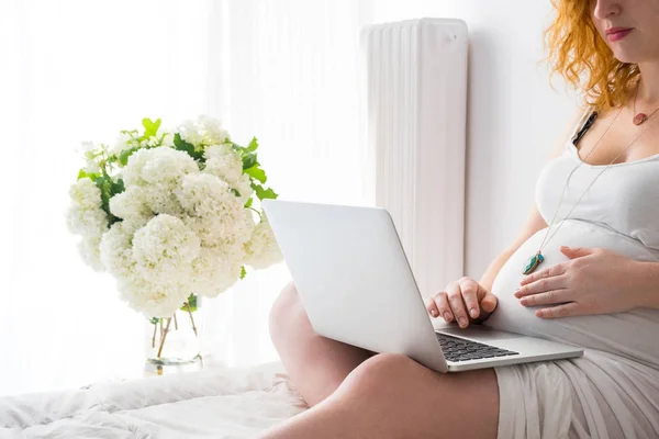 Jonge zwangere vrouw ontspannen op bed met een laptop — Stockfoto