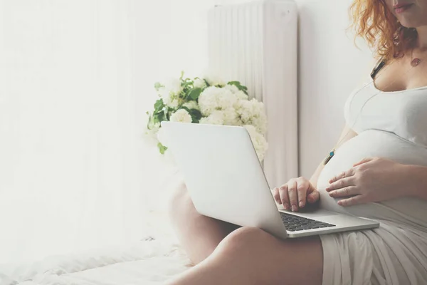 Fiatal terhes nő pihentető ágyon egy laptop — Stock Fotó