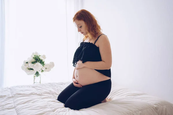 Schwangere sitzt im Bett und berührt ihren Bauch mit den Händen — Stockfoto
