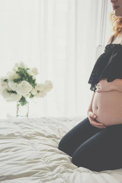 Schwangere sitzt im Bett und berührt ihren Bauch mit den Händen — Stockfoto