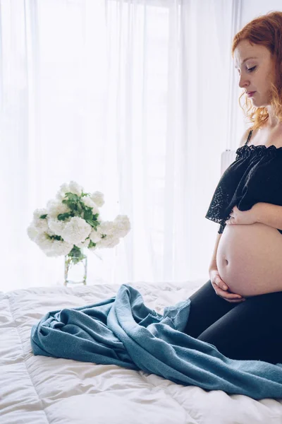 Zwangere vrouw zitten in bed en haar buik met handen aan te raken — Stockfoto