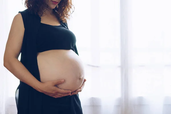 Zwangere vrouw die tegen het raam staat — Stockfoto