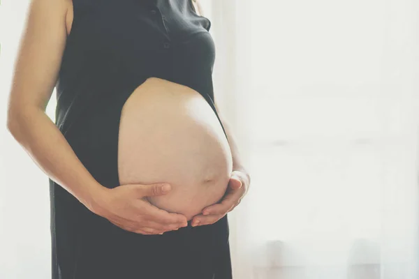 Zwangere vrouw die tegen het raam staat — Stockfoto