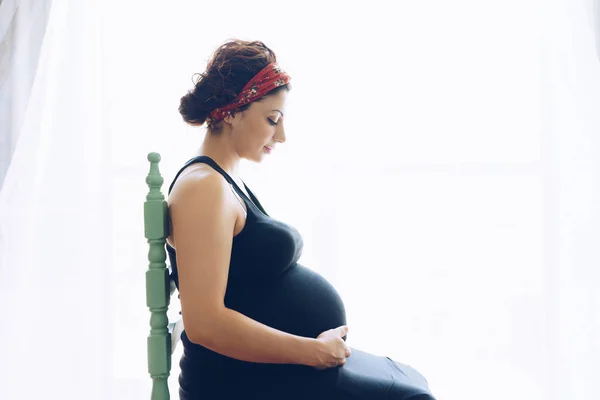 Mooie jonge zwangere vrouw zitten bij het raam in kamer — Stockfoto