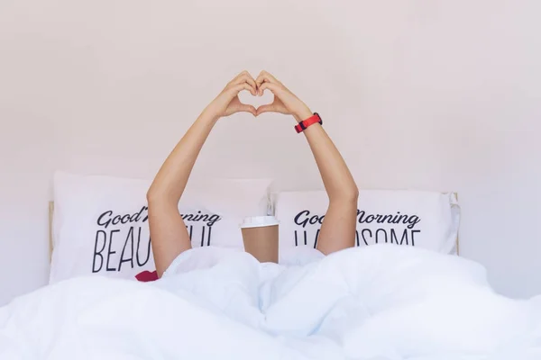 Flicka gör ett hjärta-form med händerna under täcket på th — Stockfoto