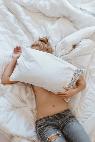 Bar överkropp kvinnan döljer ansikte med kudde liggandes i sängen — Stockfoto