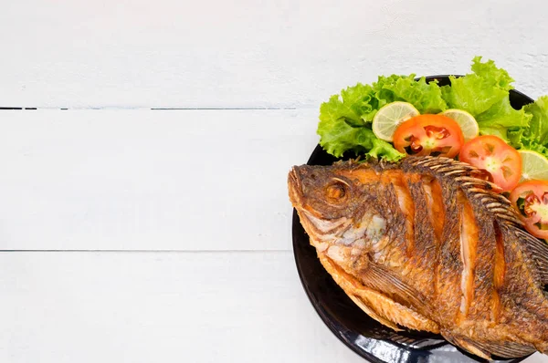 fried fish with vegetable on black dish. top view