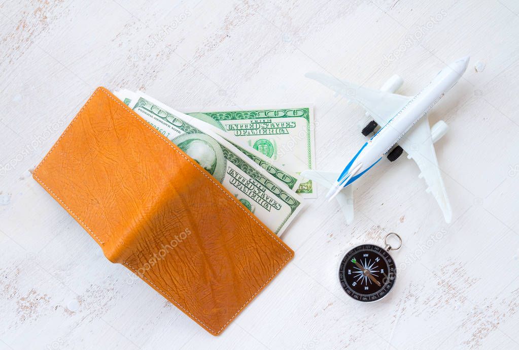 travel concept. money for travel in leather wallet with compass and aircraft toy on white wooden background
