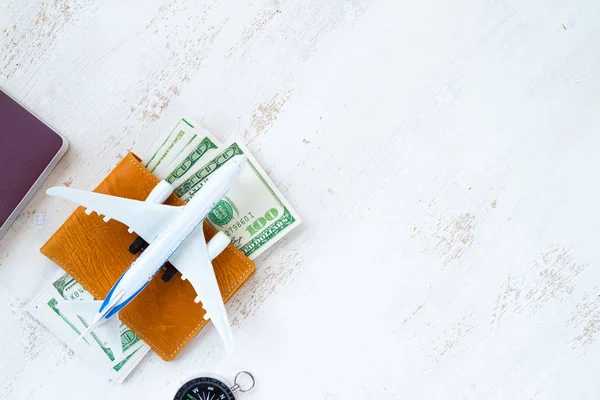 travel concept. money for travel in leather wallet with compass passport and aircraft toy on white wooden background