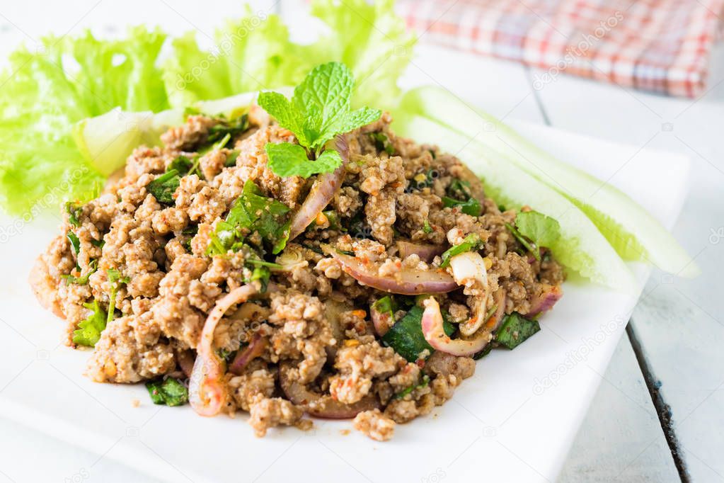 thai food. larb moo in thai name. spicy pork salad with herbs on white wooden board