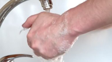 Suyun altında sabunla ellerini yıkar.