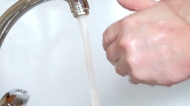 Suyun altında sabunla ellerini yıkar.