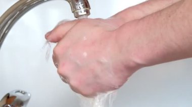Suyun altında sabunla ellerini yıkar.