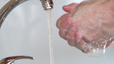 Suyun altında sabunla ellerini yıkar.