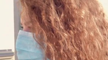 Tıbbi maskeli kıvırcık kız ağır çekimde gider.