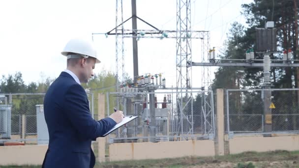 Un giovane ingegnere sullo sfondo di una centrale elettrica scrive dati su un tablet — Video Stock
