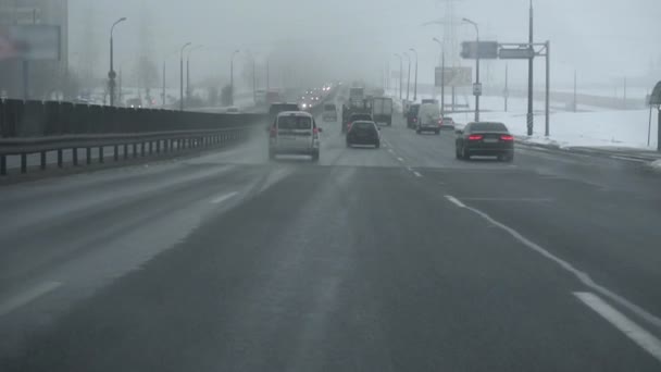 Jazda samochodem po autostradzie podczas opadów śniegu. Widok z wnętrza kabiny przez szybę przednią. Zimowy dzień. Złe warunki pogodowe dla ruchu, śnieżyca. Niebezpieczeństwo dla wycieczek. Szklany czarny lód na drodze gruntowej — Wideo stockowe
