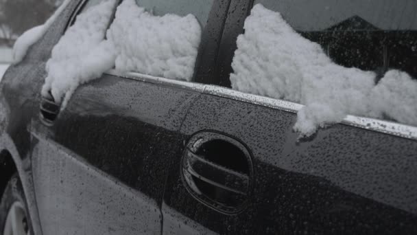 Sneeuw ligt op een auto zijruiten tijdens de sneeuwval in de winter overdag. Slechte weersomstandigheden voor het verkeer, sneeuwstorm. Gevaar voor reizen. Glazig zwart ijs op de weg. Sneeuw bedekte auto is in de tuin — Stockvideo