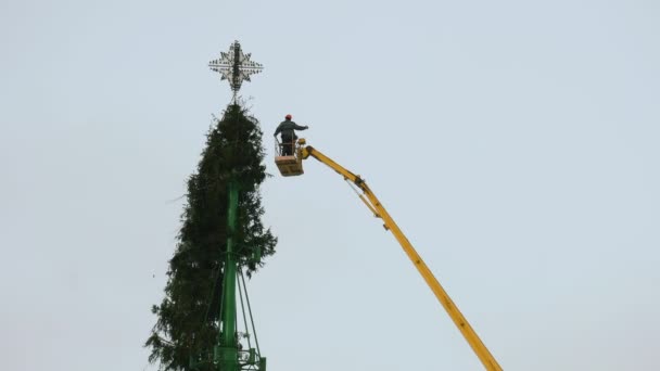 İşçiler şehrin merkez meydanında bir Noel ağacı inşaatını söküyorlar. Yeni yıl tatili ve kutlama konseptinin sonu. Hava çalışma platformu. Elle tutulur orta çekim, yakın çekim. — Stok video