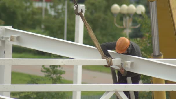 Constructeur installateur fixe un cadre métallique à une hauteur pour la construction d'un bâtiment, arrière-plan — Video