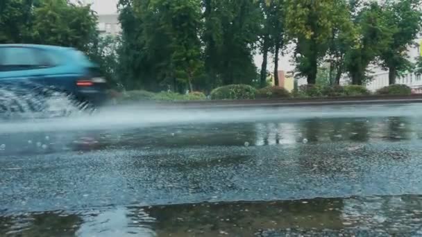 Auto 's rijden op een weg overspoeld met water, spray en fontein van onder de wielen bij regenachtig weer in de stad. Slechte en gevaarlijke omstandigheden voor het verkeer. Handheld schieten — Stockvideo