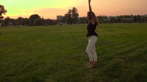 Hermosa chica caucásica con el pelo largo hace un truco en la naturaleza llamada la rueda. Fondo puesta de sol soleado, cámara lenta, acrobacias — Vídeo de stock