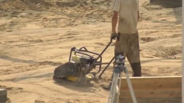 Bir erkek işçi döşeme kiremitleri için bir yol inşa edilirken kumu temizler. Toprak pıhtılaşma ekipmanları, inşaat, sanayi