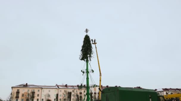 Az újévi ünnepek és ünnepségek után az emberek eltávolítják a karácsonyi koszorúkat és díszítéseket a város főterén lévő fa szerkezetéből. Légi munka platform télen. Kézzel tartott széles lövés — Stock videók