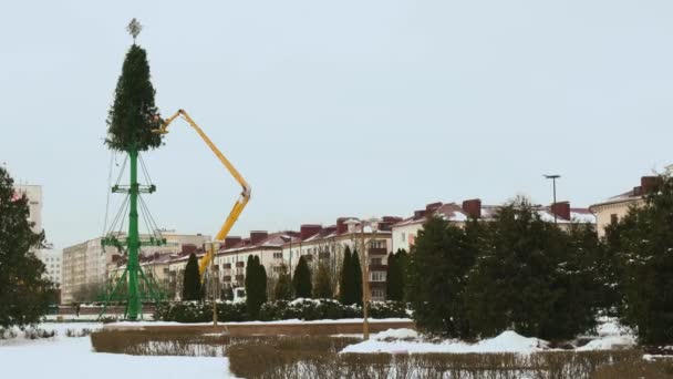 Het einde van de nieuwjaarsvakantie concept. Arbeiders ontmantelen een kerstboomstructuur op het centrale plein van de Russische stad. Feestjes. Luchtwerkplatform in de winter. Hand breed schot gehouden — Stockvideo