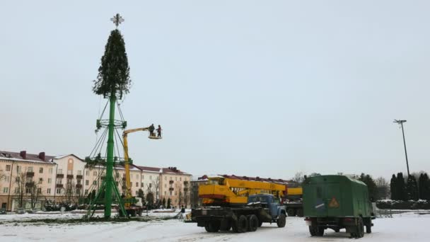 Los trabajadores desmantelan una estructura de árboles de Navidad en la plaza central principal de la ciudad después de las fiestas y celebraciones de Año Nuevo. Plataforma de trabajo aéreo en invierno. Mano de tiro ancho — Vídeos de Stock