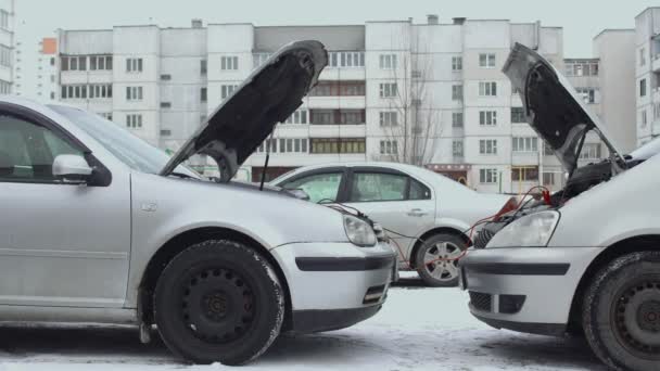 La batterie de voiture déchargée se charge à partir de la batterie automobile à l'aide de câbles de serrage de cavalier connectés à la borne postale. Hottes levées en hiver de jour dans le stationnement. Dysfonctionnement ou problème avec l'auto. Partie 5 — Video