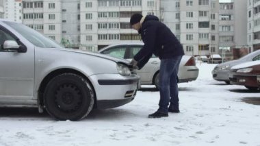 Adam kışın otoparkta arabasının kaputunu açmaya çalışıyor ama açamıyor. Bonnet soğuk hava nedeniyle dondu. Arıza ya da otomatikle ilgili bir sorun. Çöküş. Biri boşaltılan pili şarj etmek istiyor.