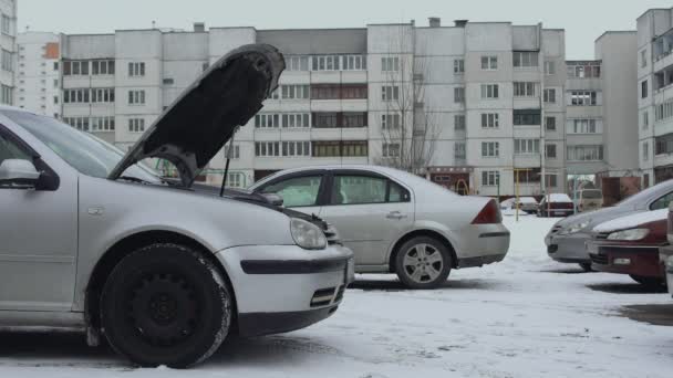 Bilen drar upp till trasig bil för att hjälpa och ladda urladdat bilbatteri. Hood växte upp på vintern dagtid på parkeringen av gården. Man vill ladda urladdat batteri med hjälp av kablar. Del 1 — Stockvideo