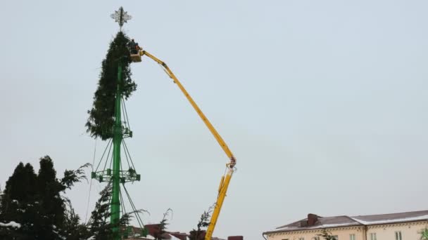 Les gens démontent une structure d'arbre de Noël sur la place centrale principale de la ville. Le concept des fêtes de fin d'année. Des célébrations. Plateforme de travail aérien en hiver. Plan large tenu à la main — Video