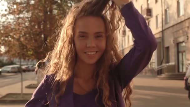 Mooi jong meisje met lang krullend haar op de achtergrond van de zon, close-up, slow motion. Haarverzorging — Stockvideo