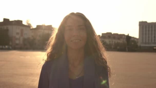 Young beautiful girl without makeup with natural beauty in the city. Video portrait of a girl with long curly hair on a sunset background, slow motion, caucasian — Stock Video