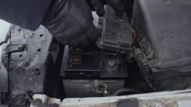 Adam kışın tamir etmek ya da tamir etmek için arabadan boşaltılmış aküyü çıkarıyor. Arıza ya da otomobille ilgili bir sorun. Kaput ya da kaput gündüz vakti park yerinde kalkıyor. Kurşun asitli akünün kapanışı