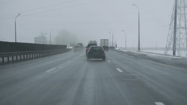 Auto menee radalle lumimyrskyn aikana. Näkymä ohjaamosta tuulilasin läpi. Talvipäivän lumisade. Huonot sääolosuhteet liikenteelle. Vaara matkoilla. Lasimainen musta jää maantiellä — kuvapankkivideo