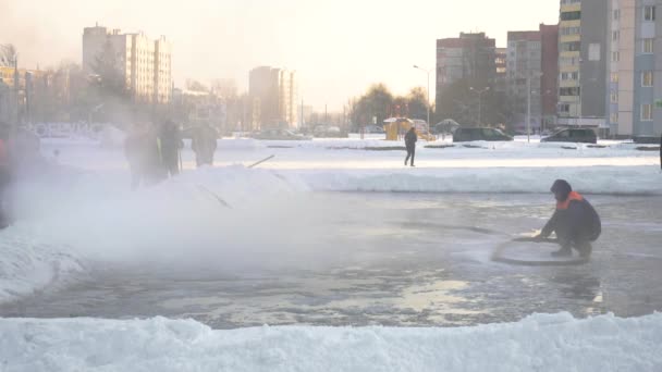 Il lavoratore dei servizi comunitari versa acqua per fare una pista di pattinaggio su ghiaccio durante la giornata soleggiata invernale. Rallentatore — Video Stock