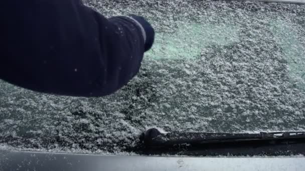 Man paints a sad smiley emoji on snow covered rear windshield or windscreen in winter daytime. Bad and cold weather. — Stock Video