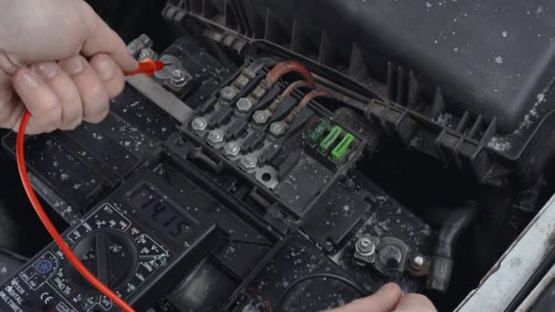 Man measures DC voltage on terminals of automotive battery using multimeter in winter daytime in parking. Malfunction or problem with automobile. Hood or bonnet raised up. Closeup of lead-acid battery — Stock Video