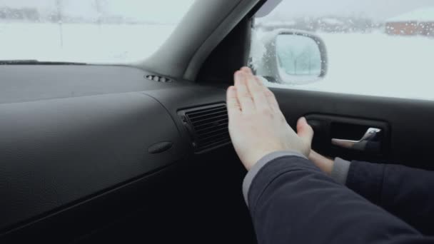 Man inside the car warms his hands from the cold using air heat conditioner stove in winter daytime. One froze outside. Bad and cold weather. — Stock Video