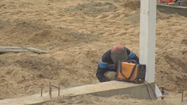 Um homem usando uma máquina de solda solda superfícies metálicas em um canteiro de obras, espaço de cópia, indústria — Vídeo de Stock