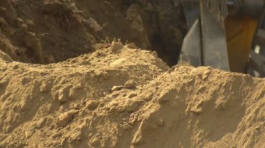 Traktör yükleyicisi inşaat sırasında büyük bir kovada toprak kazanıyor, yakın plan. İnşaat ve yol mühendisliği, endüstri, geçmiş