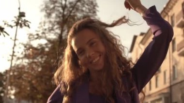 Kıvırcık saçlı ve koyu tenli genç bir kız güneşli bir günbatımının arka planına gülümsüyor. Yavaş çekim, parla