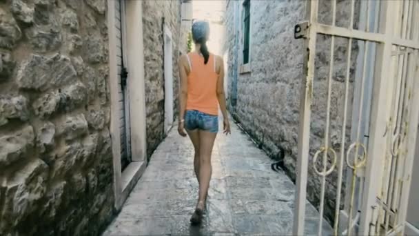 Flicka turist promenader längs smal kullerstensgata bland gamla tegelhus av venetianska och medelhavsarkitektur i medeltida staden Budva stad i Montenegro som Italien eller Kroatien. Turistresa, Resor — Stockvideo