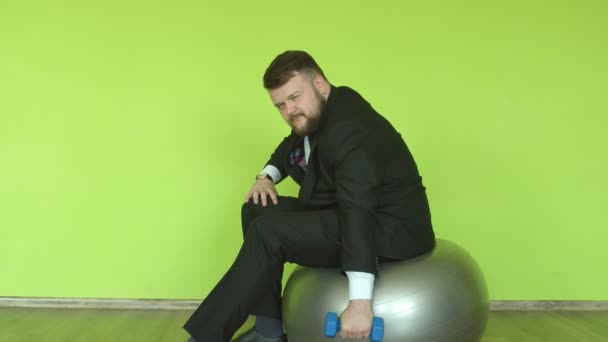 Um homem caucasiano em um terno de negócios com barba está envolvido com um haltere no ginásio em um fundo verde, espaço de cópia — Vídeo de Stock