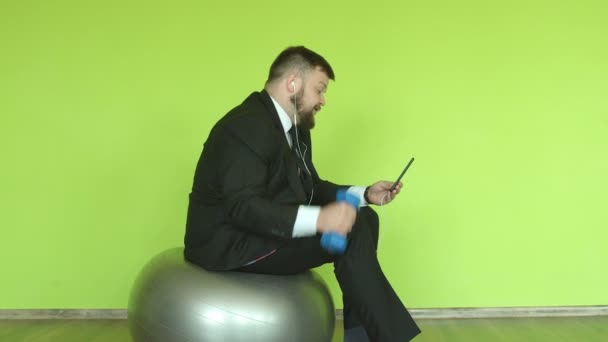Sakallı bir ofis çalışanı ile beyaz bir adam telefonda video bağlantısıyla konuşuyor ve spor yapıyor, yeşil arka plan, kromackey. — Stok video